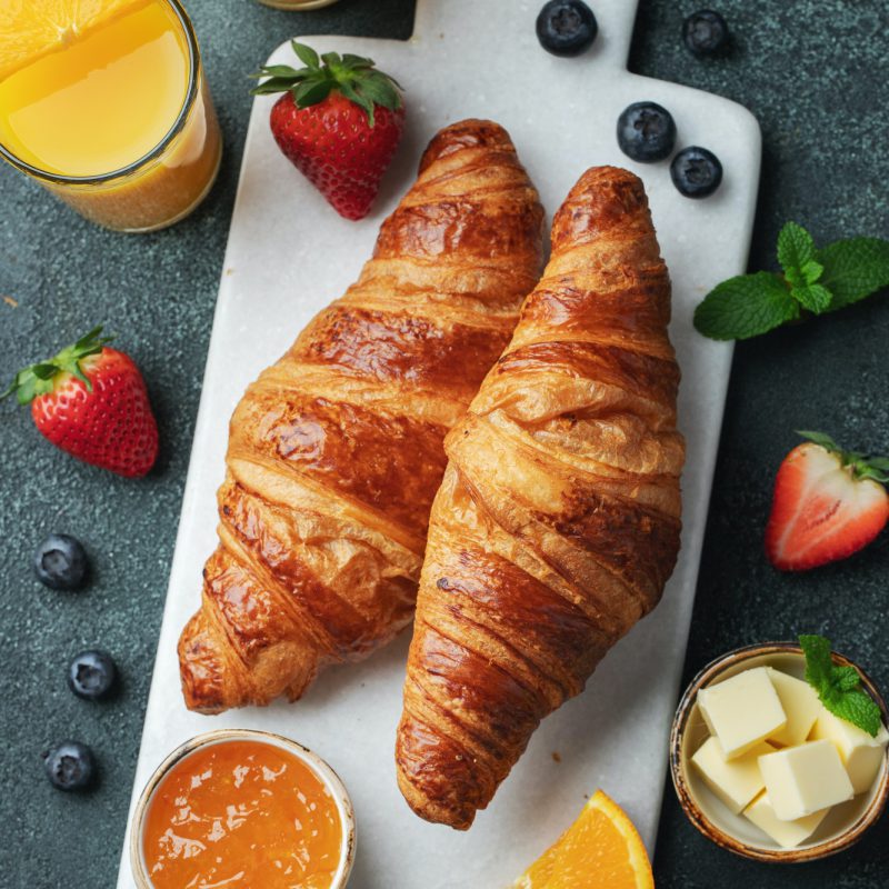 Fresh sweet croissant with butter for breakfast. Continental breakfast on a dark concrete table.